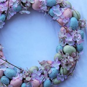 A wreath laced with brightly colored flowers and eggs sat on a light blue surface.