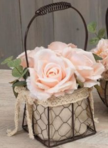 A wired basket lined with cloth and lace with light pink roses inside.
