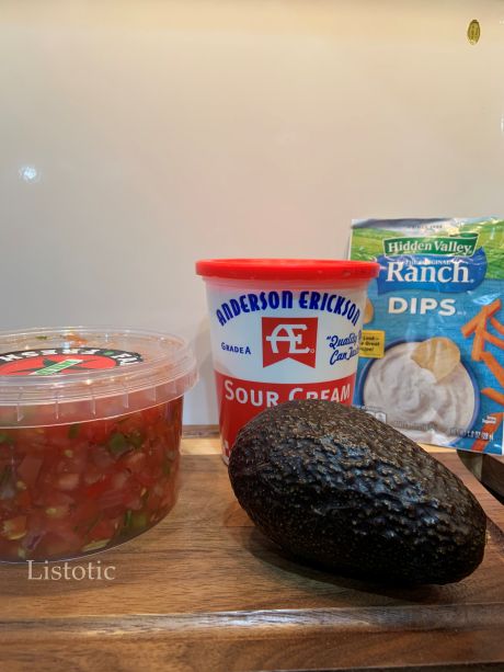 An ingrediend lineup consisting of fresh salsa, sour cream, an avocado, and a packet of dry ranch.