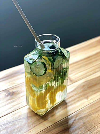 Pitcher of water filled to the brim with healthy fresh fruits and veggies being stirred with a wooden spoon. 