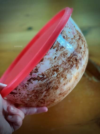 Plastic bowl with a lid being used to shake the homemade powdered sugar and coat the no bake snacks is a easy method to no bake snacks