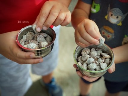 Kids hands picking up pieces of a peanut butter snack mix puppy chow recipe out of a small metal snack bowl