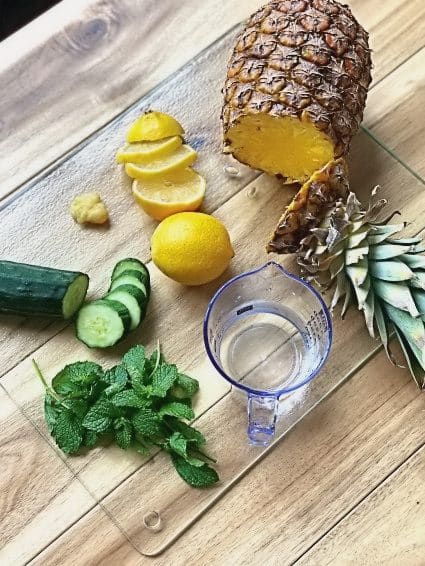 Pineapple, lemon, cucumber, mint chopped up on a cutting board for a detox drink