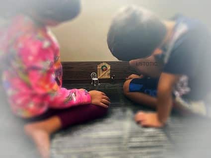 two children looking at an elf door on the trim of a wall trying to find the elf foot prints 