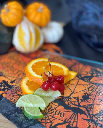 cocktail garnishes of cherries, sliced oranges and sliced lime sitting on a Halloween table cloth
