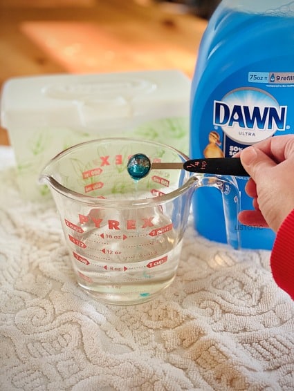 Dawn dish soap being added to a measuring cup of rubbing alcohol for kitchen wipes