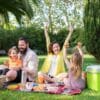 an excited family of four having a picnic outside in the grass