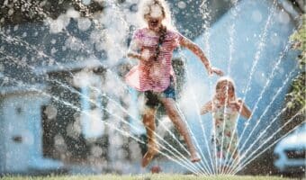 girl running through sprinkler to cool off on a hot summer day